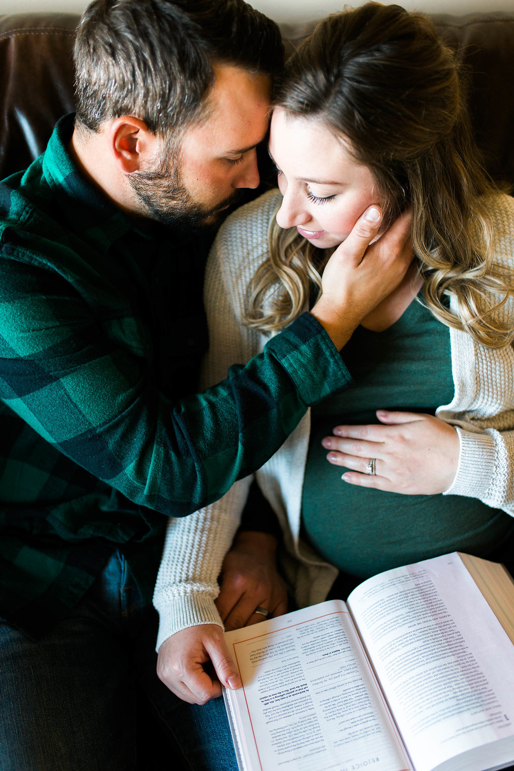 a couple reading a bible and looking down on the wife's pregant belly
