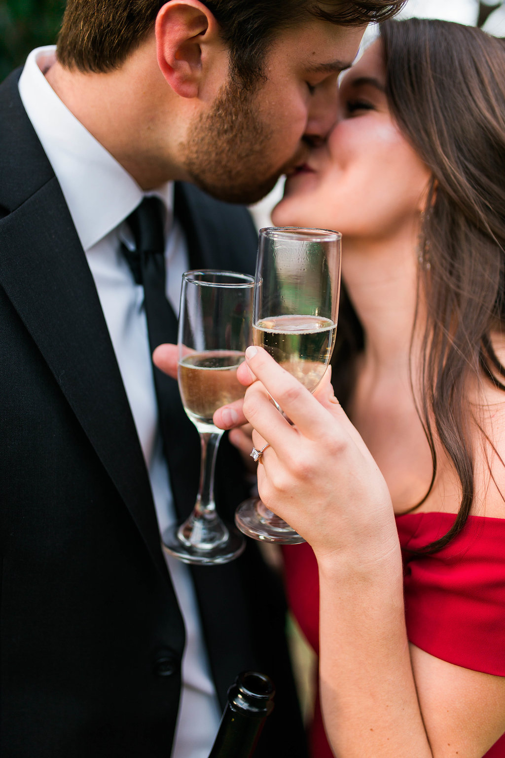 a newly engaged couple clinking champaign glasses while kissing