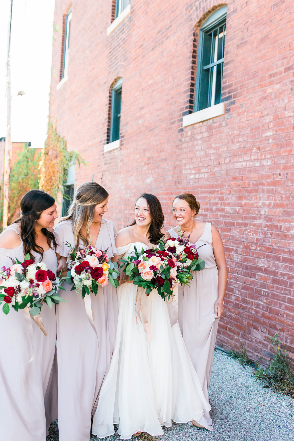 three bridesmaids in light pink dresses and a bride all holding rose bouquets and laughing with eachother
