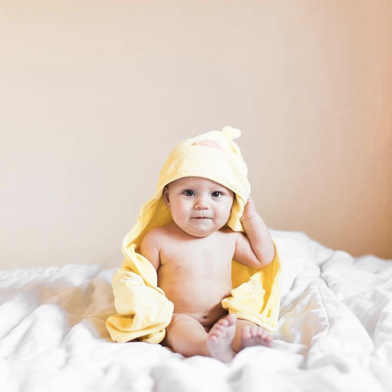 7 month old Ellis sitting on a bed wrapped in a yellow duck towel
