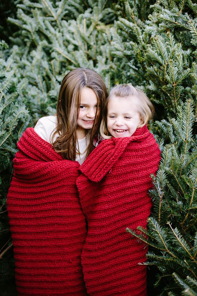young sisters wrapped in a red blanket infront of pine trees
