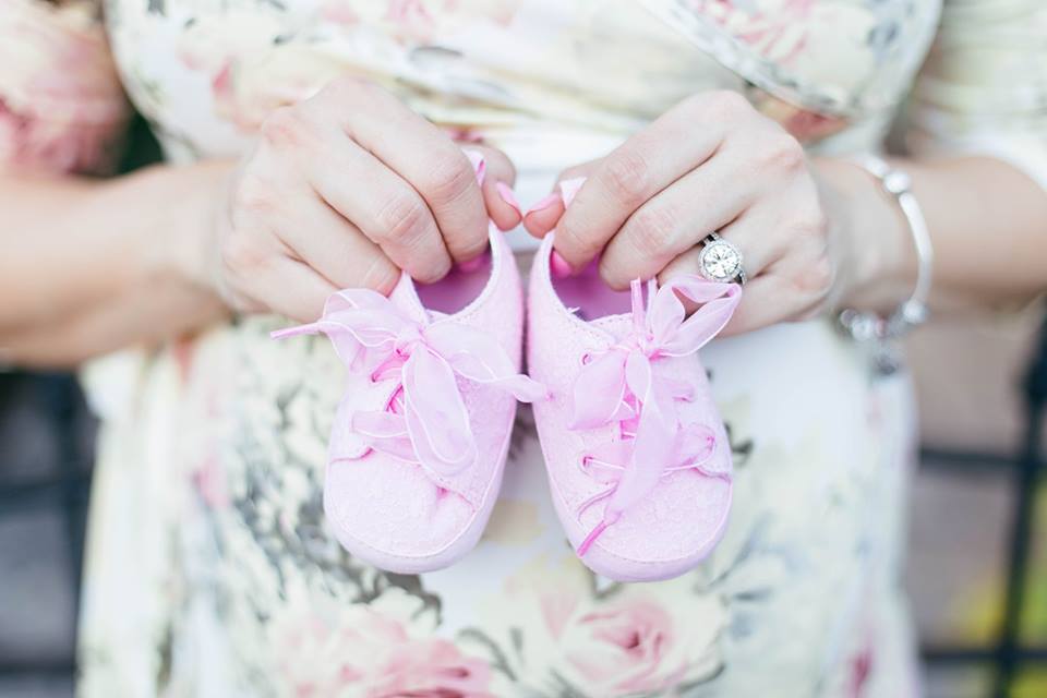 a pregnant woman holding pink baby shoes infront of her belly