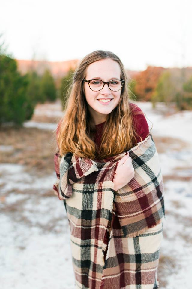 a senior girl wrapped in a red plaid blanket smiling for the camera