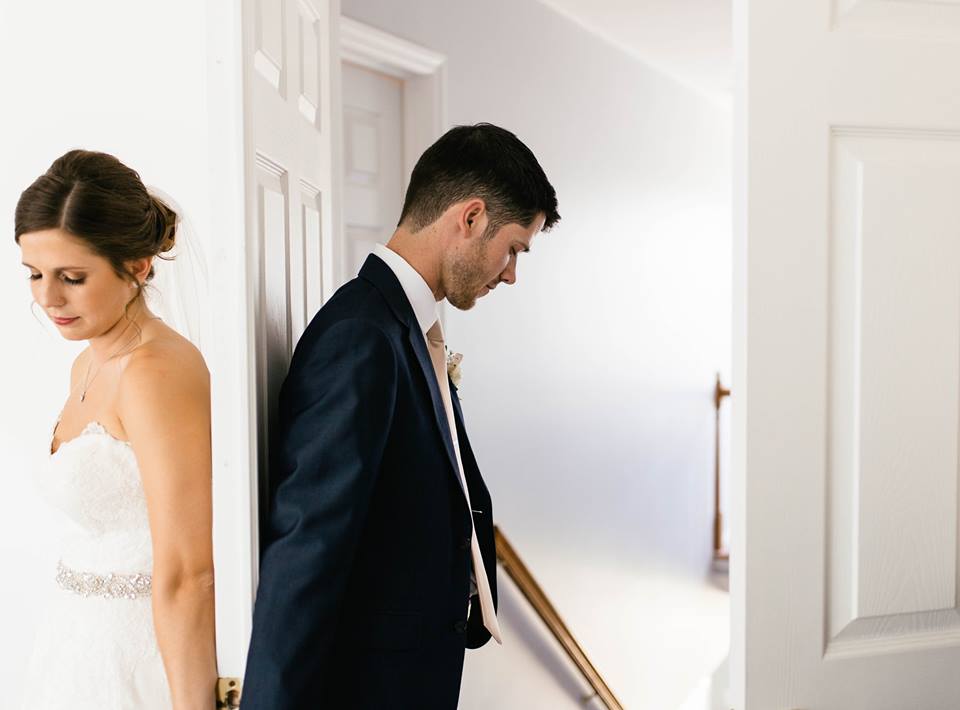 a bride and groom on oposite sides of a door, holding hands and praying