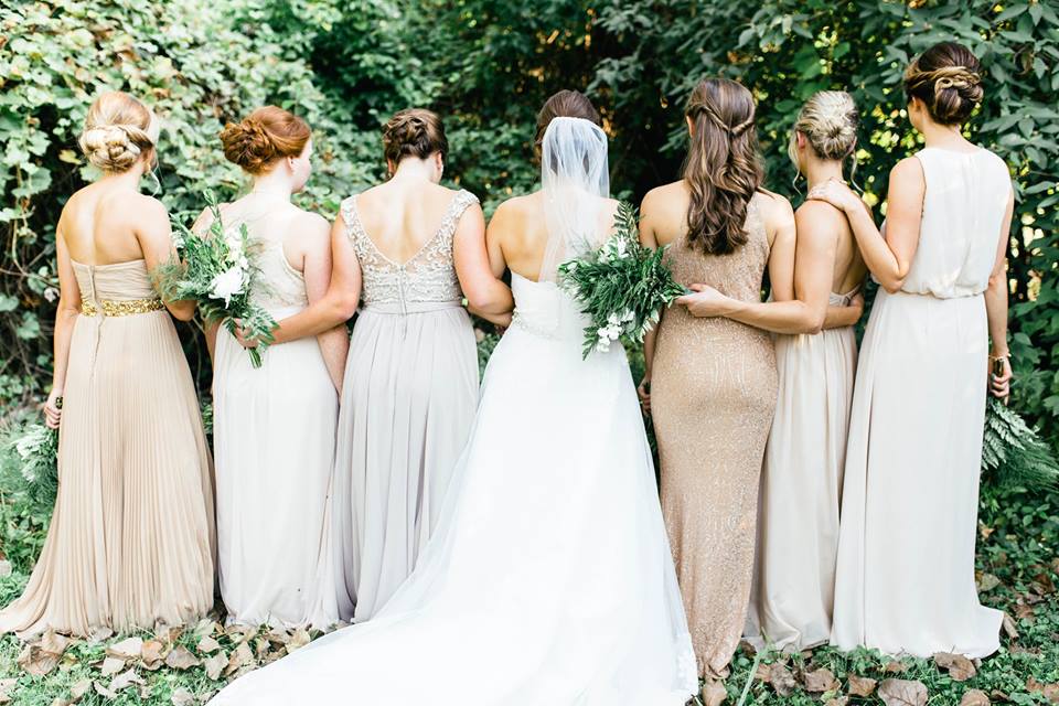 six bridesmaids in champaign colored dresses with a bride in the middle, with their backs turned to the camera